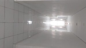 A long, narrow hallway with white tiled walls and a shiny floor, leading to a bright exit. - Studio Room Apartment Aeropolis by Rusdi (Tangerang)