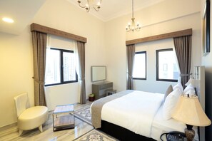 Relax in a spacious room with a large bed, desk, and TV, surrounded by natural light and a comfortable seating area.