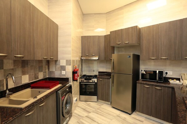 Enjoy cooking in this well-lit kitchen with sleek cabinetry, a refrigerator, oven, and microwave.