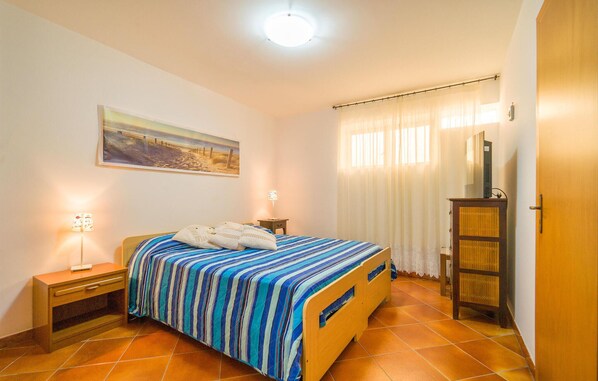 A bedroom with a bed, a nightstand, a lamp, a painting, a wardrobe, and a window with curtains.