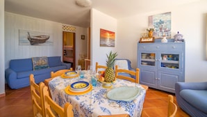 A dining area with a table set for four, surrounded by wooden chairs. There is a blue sofa in the background and a cabinet with glass doors containing kitchenware. - 3 bedroom awesome home in Menfi (Menfi)