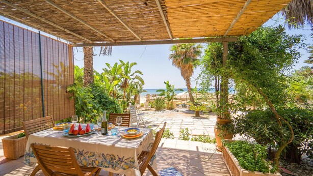 An outdoor dining area with a table set for two, surrounded by lush greenery and a view of the beach. - 3 bedroom awesome home in Menfi (Menfi)