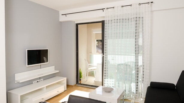 Uma sala de estar moderna com uma televisão de tela plana, estantes brancas, uma mesa de centro de vidro e um sofá preto.