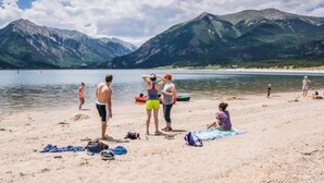 Ein Strand mit Bergen im Hintergrund, Menschen liegen in der Sonne, und ein See.