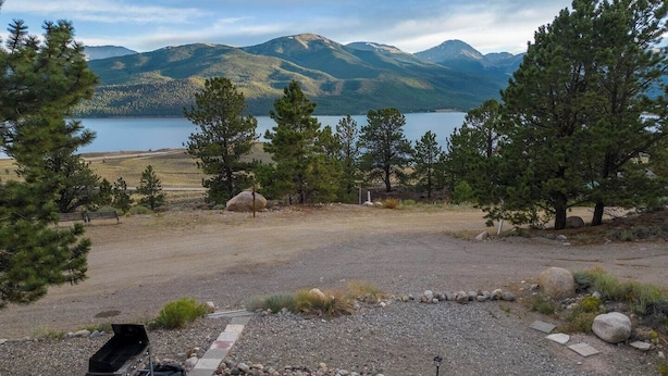 Un camping con una parrilla, una mesa de picnic y vistas panorámicas de montañas y un lago.