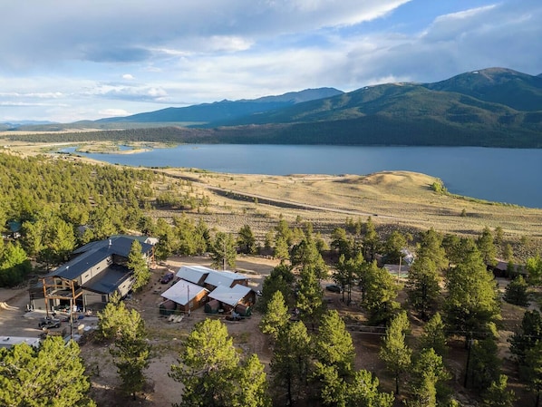Una cabaña con cabañas y un lago grande, rodeada de montañas y un bosque denso.