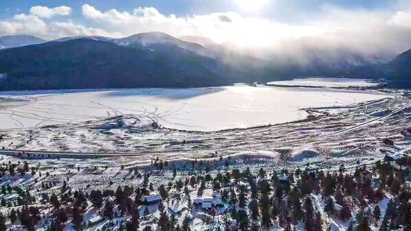 Una vista panorámica de un paisaje invernal con un lago, campos nevados y montañas al fondo.