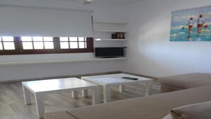 A modern living room with a beige sofa, two white coffee tables, a flat-screen TV on a shelf, and a painting on the wall. - Son Bou Apartments (Alayor)
