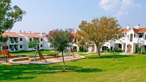 A courtyard with white buildings, a playground, and a well-maintained lawn. - Son Bou Apartments (Alayor)