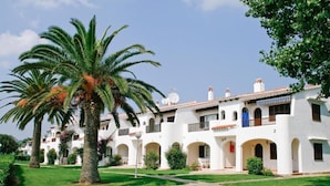 A white building with multiple balconies and arches, surrounded by well-maintained lawns and palm trees. - Son Bou Apartments (Alayor)