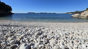 A pebble beach with clear blue water and distant hills. - Indy's Beach Apartments (Dubrovnik)