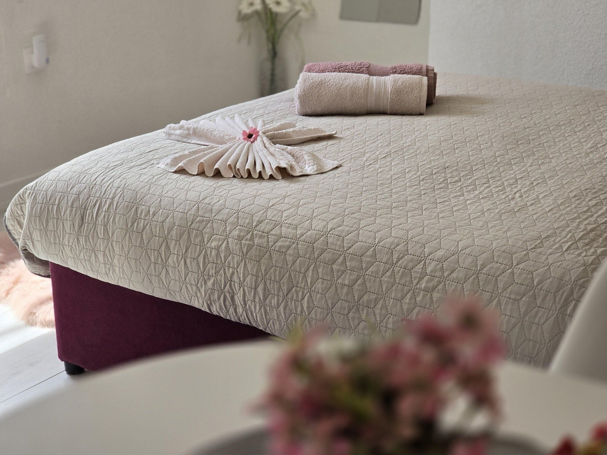 A neatly made bed with a quilted cover, a folded towel, and a decorative arrangement of towels on the bed.