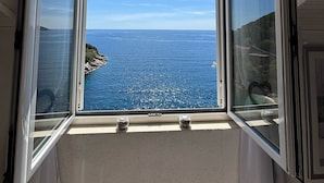 A room with a large window overlooking a coastal view. - Indy's Beach Apartments (Dubrovnik)
