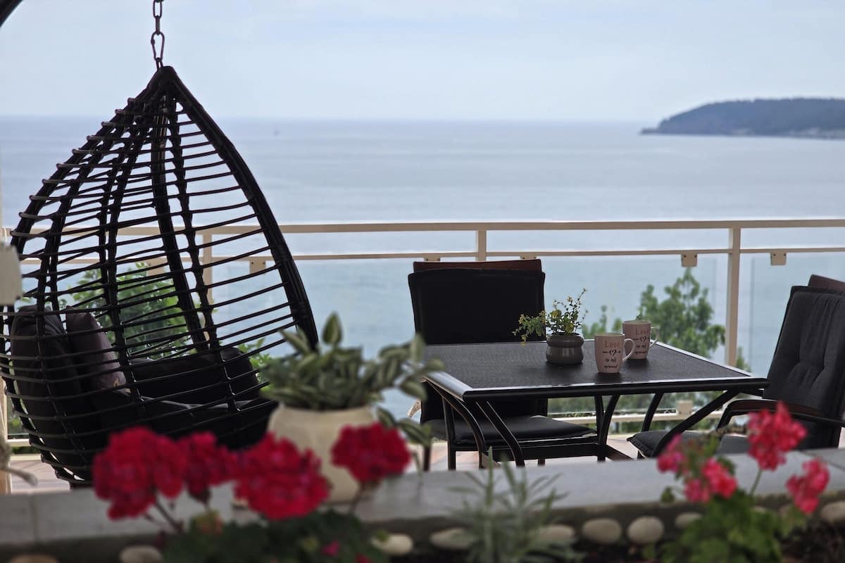 A balcony with a hanging chair, a table, and potted plants.