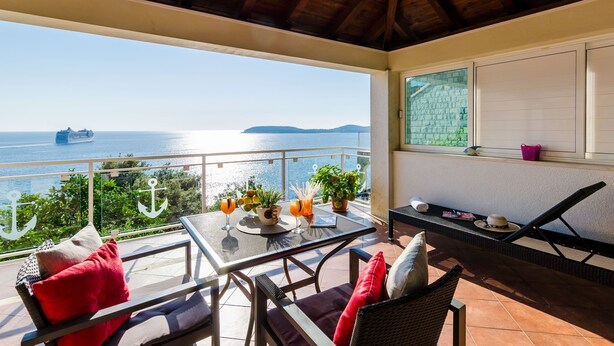 A balcony with a table set for two, a chair, and a sun lounger. - Indy's Beach Apartments (Dubrovnik)
