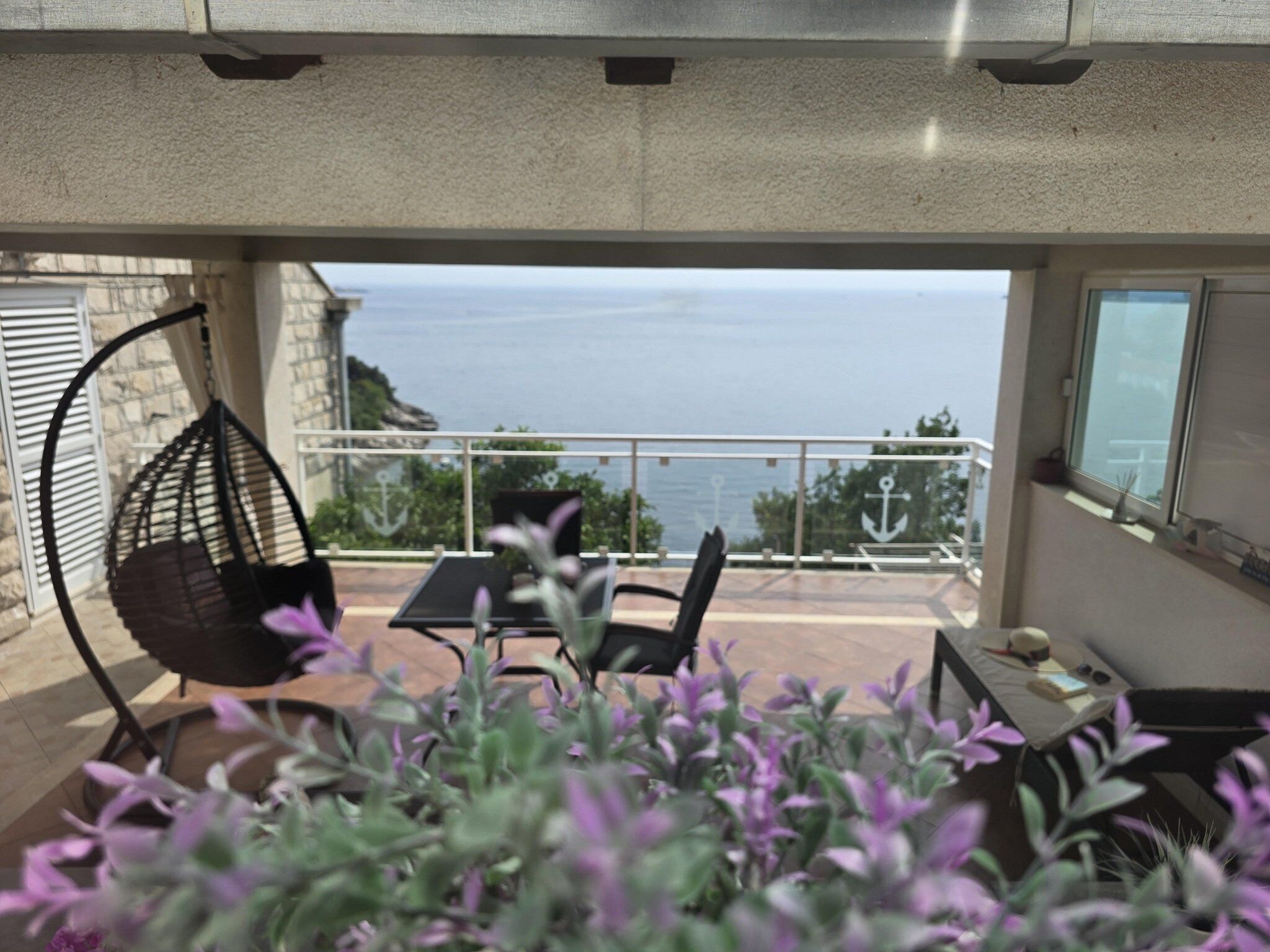A balcony with a hanging chair, a table, and a view of the sea.