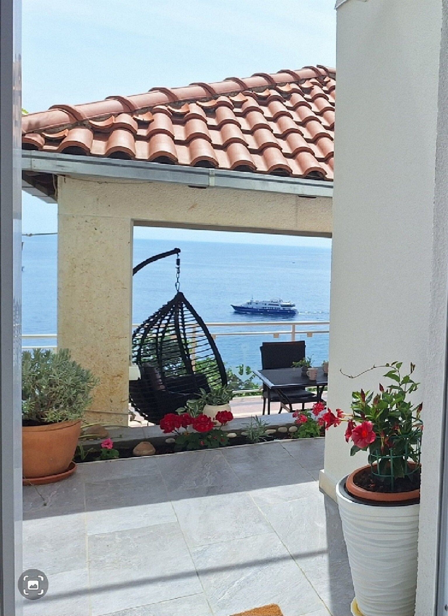 A patio with a hanging chair, a table, and potted plants.