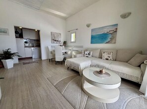 A spacious living area with a sofa, a dining table, and a kitchen in the background. - Indy's Beach Apartments (Dubrovnik)