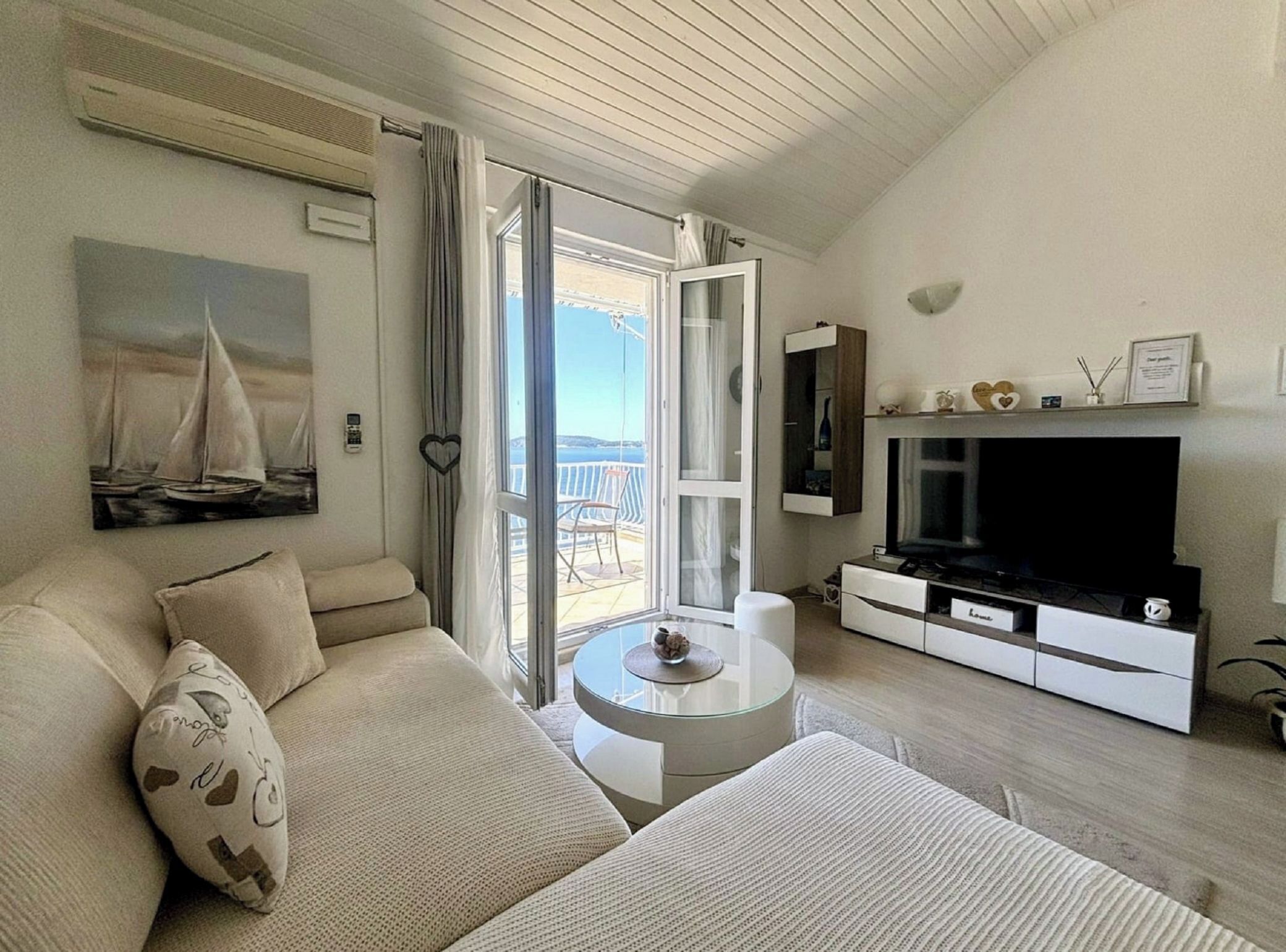 A living room with a sofa, a coffee table, a TV, and a balcony with a view.