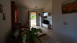 Olohuoneessa on sohva, ruukussa oleva kasvi ja televisio. Ovesta pääsee parvekkeelle.