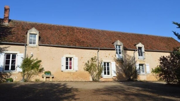 A two-story building with a red-tiled roof, multiple windows with shutters, and a small garden area with a bench. - **Spacious Gîte Near Argenton-sur-Creuse: 2 Houses, Garden, Parking, Family-Friendly** (Argenton-sur-Creuse)