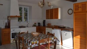A kitchen with wooden cabinets, a dining table with a checkered tablecloth, a hanging light fixture, and a clock on the wall. - **Spacious Gîte Near Argenton-sur-Creuse: 2 Houses, Garden, Parking, Family-Friendly** (Argenton-sur-Creuse)