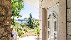 A stone wall with potted plants and a view of a lake and hills. - Apartments Lovro (Dubrovnik)