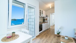 A modern kitchen with white cabinets, a wooden countertop, and a view of the sea through a large window. - Apartments Lovro (Dubrovnik)
