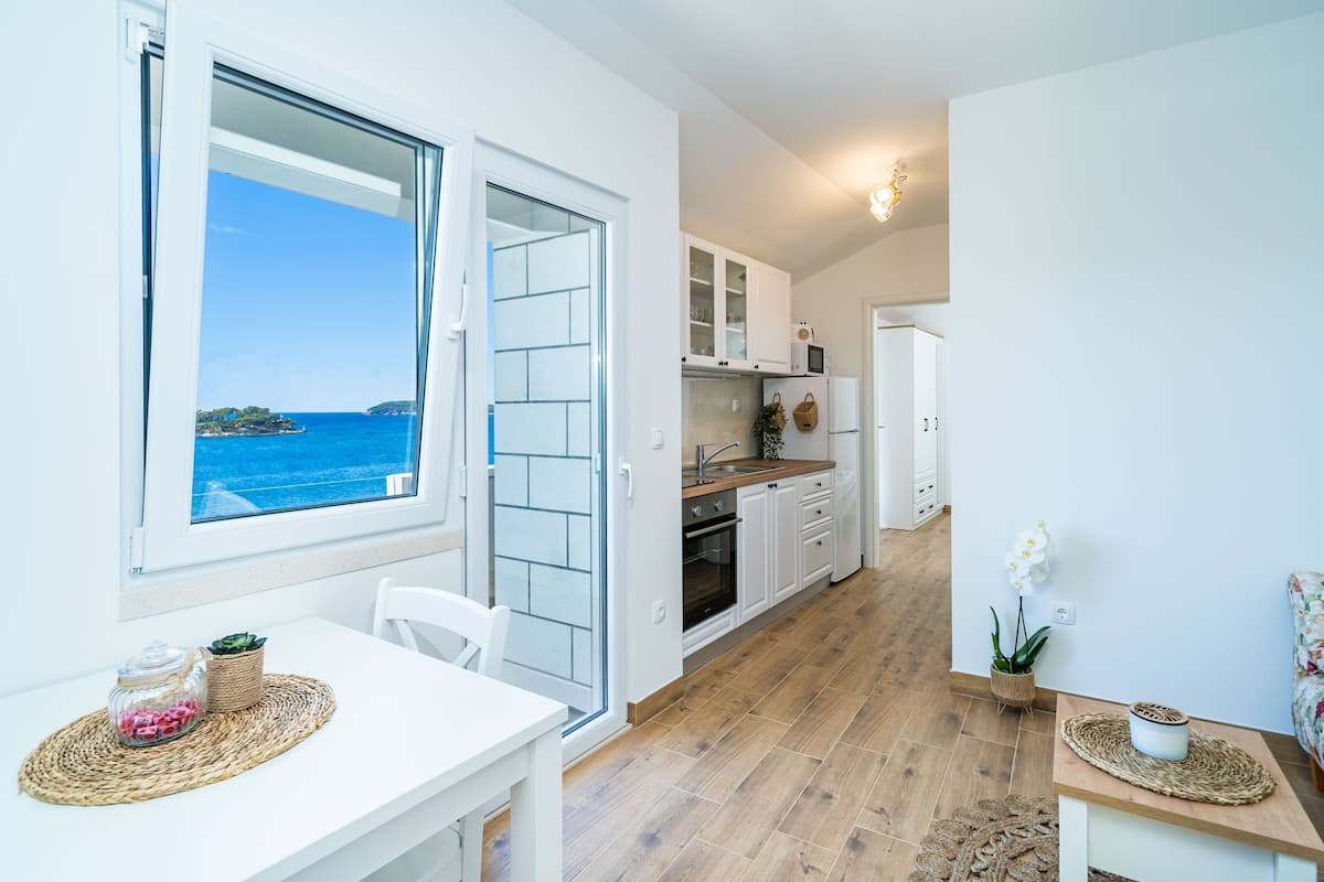 Una cocina moderna con armarios blancos, encimera de madera y vistas al mar a través de un ventanal grande.