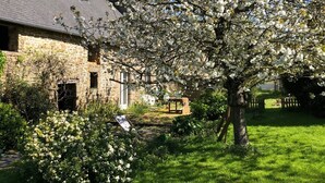 A stone building with a sloped roof, surrounded by a well-maintained lawn and flowering trees.