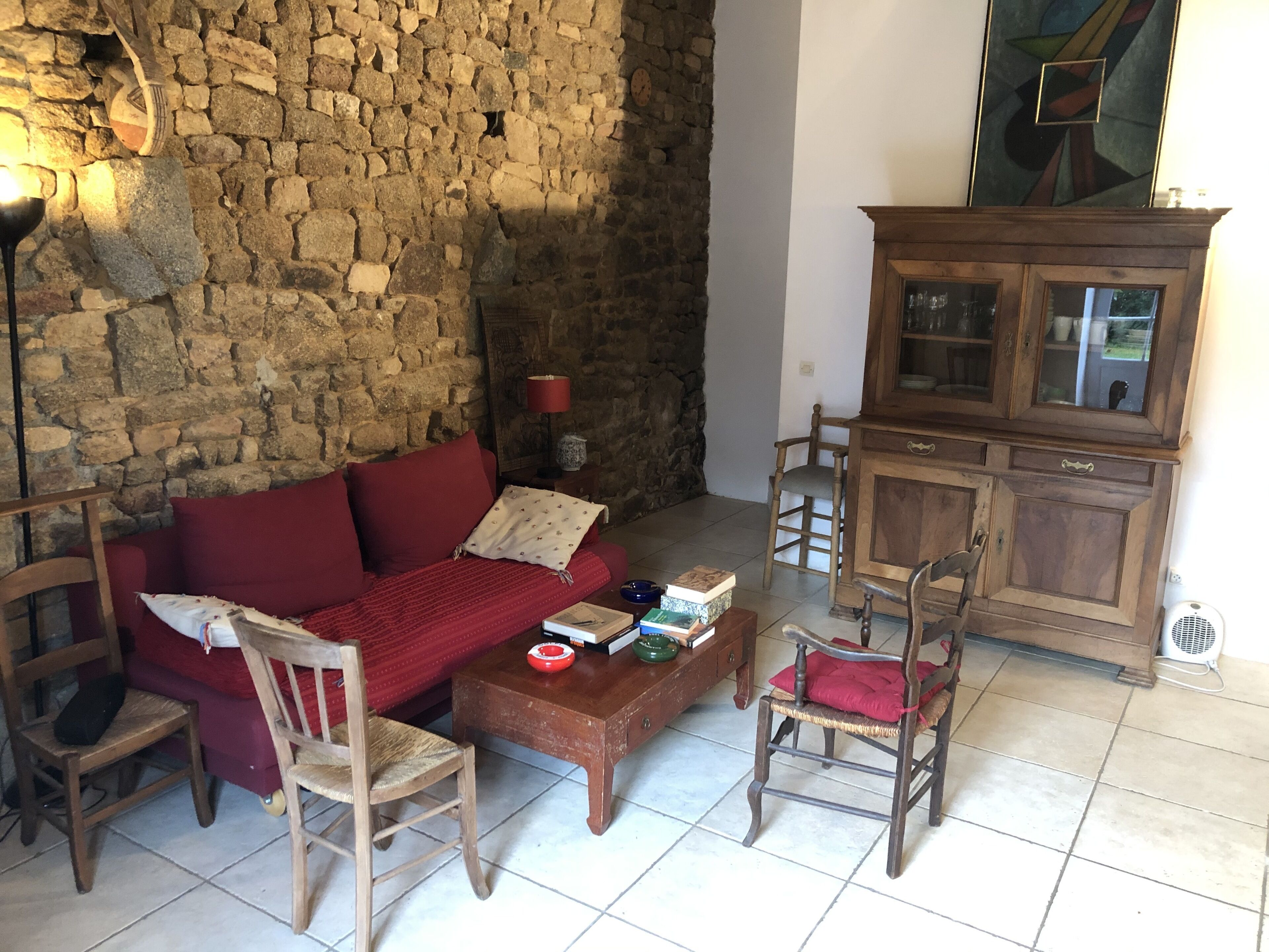 Un accogliente soggiorno con parete in pietra, un divano rosso, sedie in legno, un tavolino con libri e un mobile.