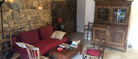 Un accogliente soggiorno con parete in pietra, un divano rosso, sedie in legno, un tavolino con libri e un mobile.