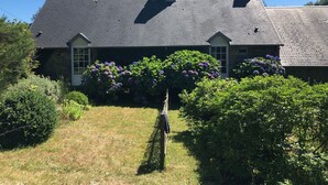 A two-story house with a dark roof, stone chimneys, and a garden with hydrangea bushes.
