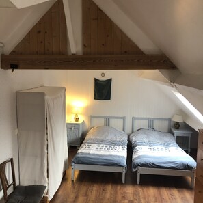 Ein kleines, gemütliches Schlafzimmer im Dachgeschoss mit zwei Betten, Holzbalken, einem kleinen Tisch mit einer Lampe und einem Stuhl.