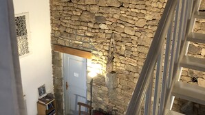 A room with a stone wall, a red sofa, a wooden chair, and a staircase.