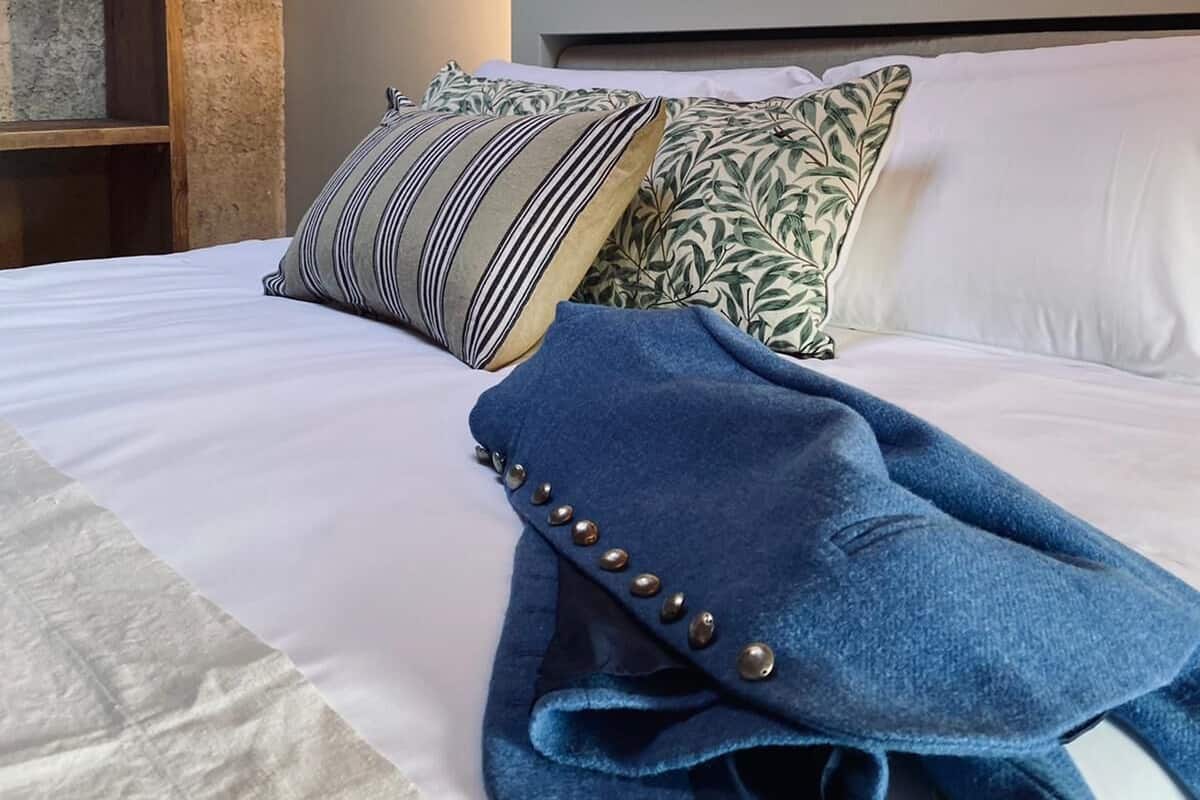 A neatly made bed with striped and leaf-patterned pillows, a blue throw blanket with buttons, and a wooden headboard.