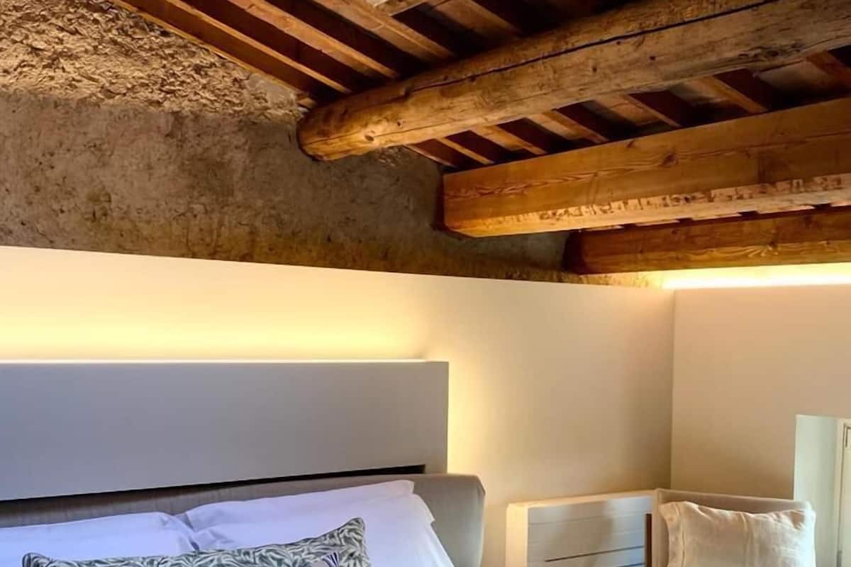 A bedroom with a wooden ceiling, a bed with white bedding, striped pillows, and a blue blanket.