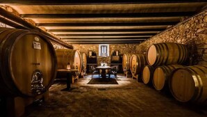 A cellar with wooden barrels arranged on stone walls, a central table, and a stone ceiling. - Corte Massimago (Mezzane di Sotto)