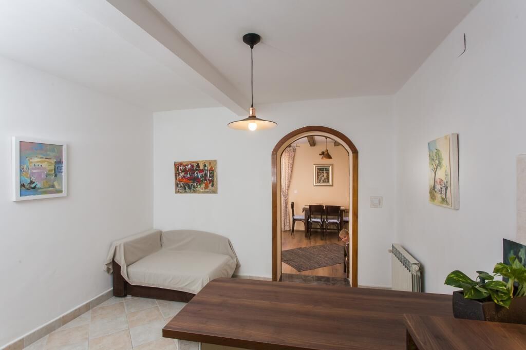 A room with a bed, a dining table, and a kitchen area visible through an archway.