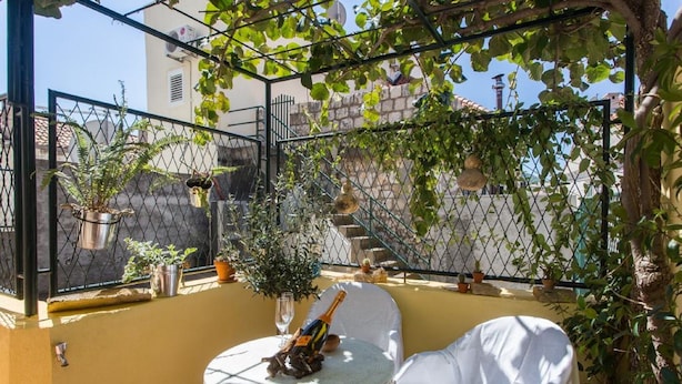 Een zonnig terras buiten met een ronde tafel, een witte stoel en potten met planten.
