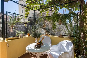 A sunlit outdoor patio with a round table, a white chair, and potted plants. - Apartment Hladilo Nostalgia (Dubrovnik)