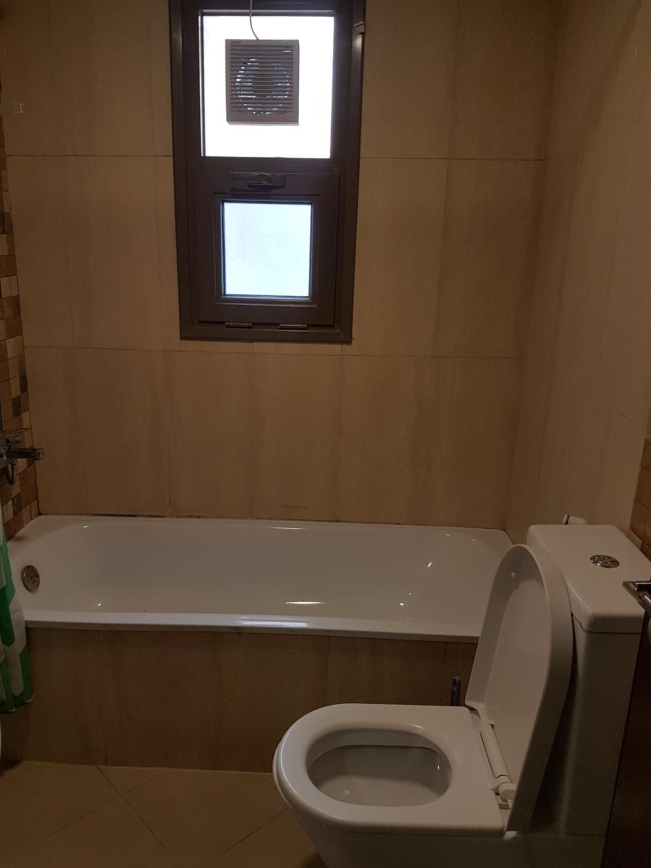 A bathroom with a bathtub, toilet, and a window with blinds.