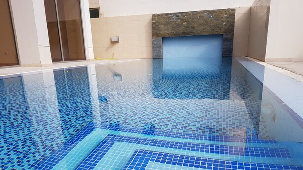 A swimming pool with blue mosaic tiles, a stone wall, and a window. - Magic Suite ALMahboula 2 (Mahboula)