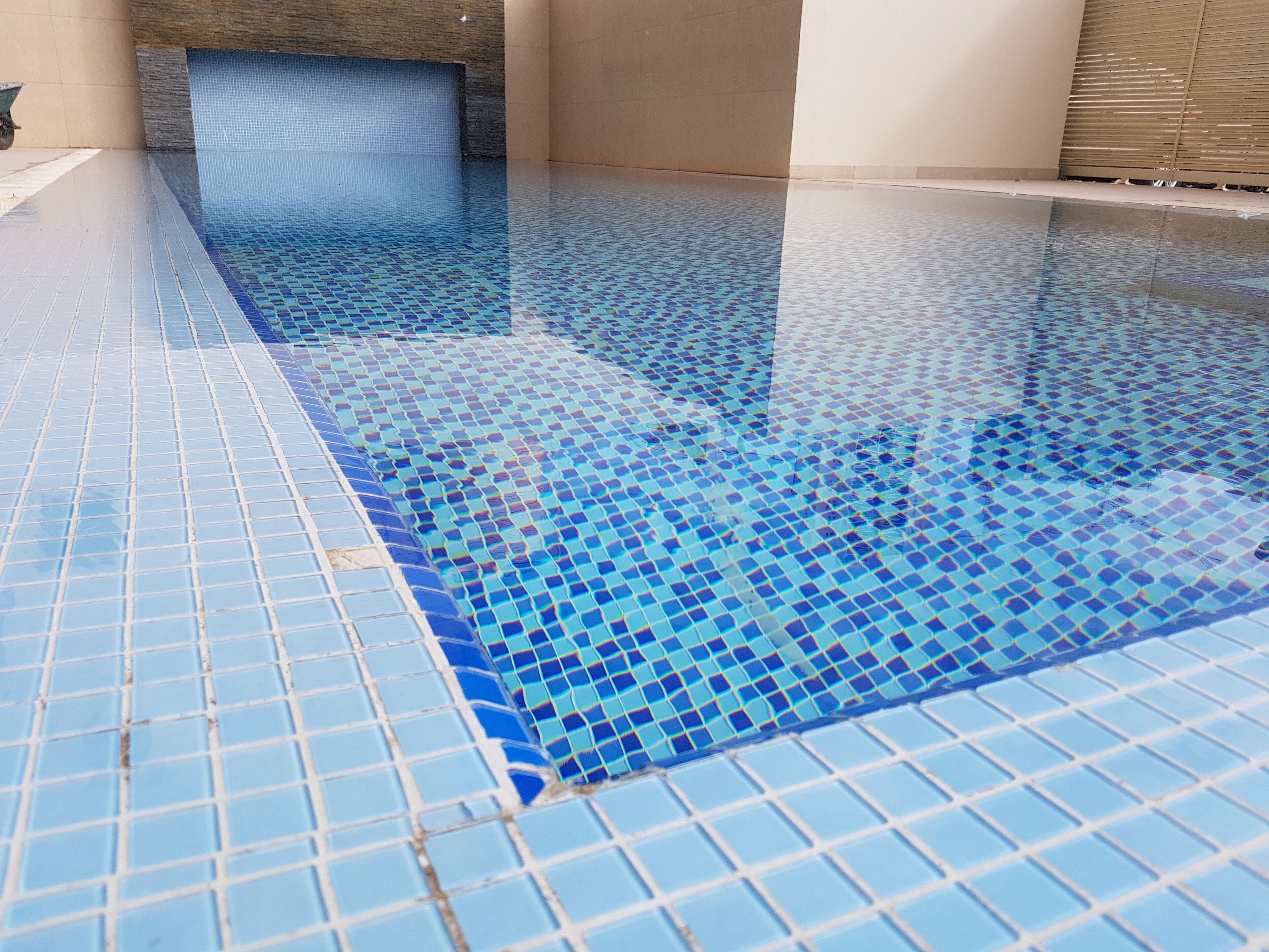 A swimming pool with a tiled floor and walls, and a small waterfall feature.