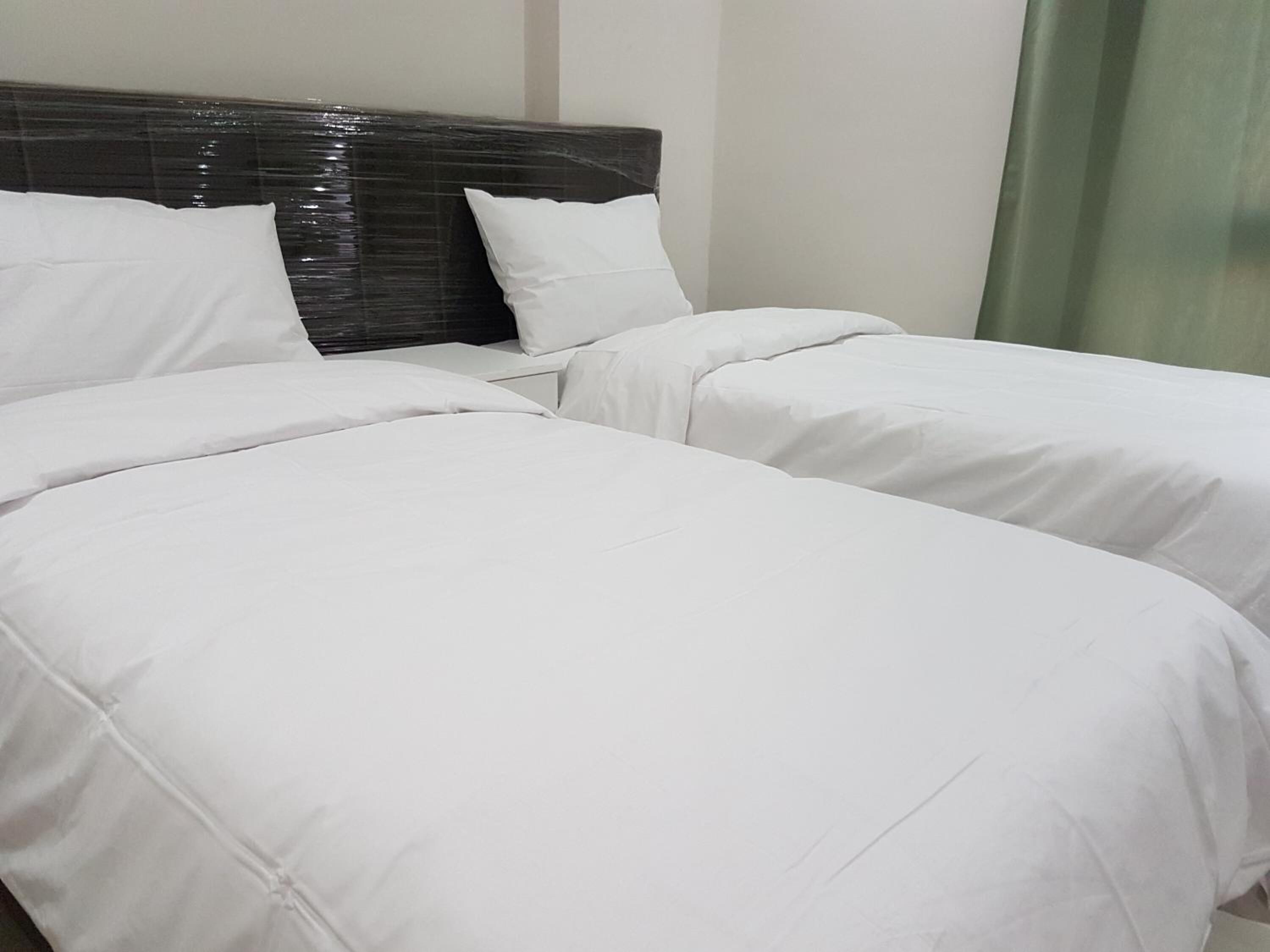Habitación de hotel con dos camas individuales, cabecera oscura y ropa de cama blanca.