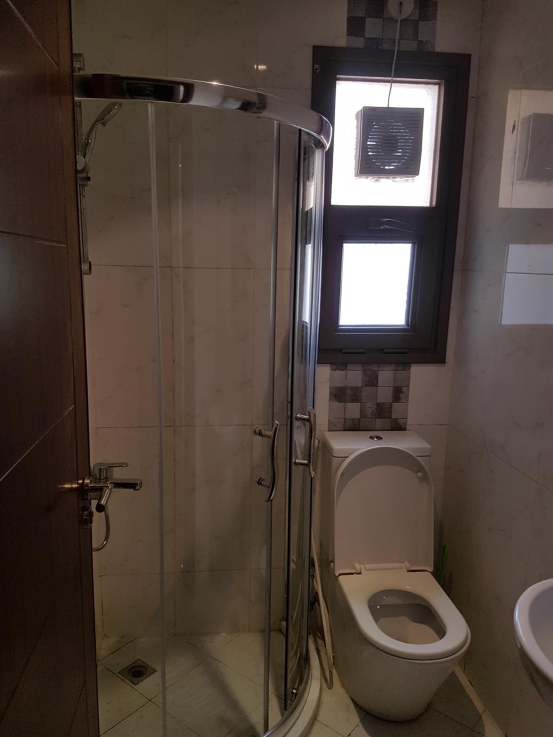 A bathroom with a glass-enclosed shower, a toilet, and a window above the toilet.