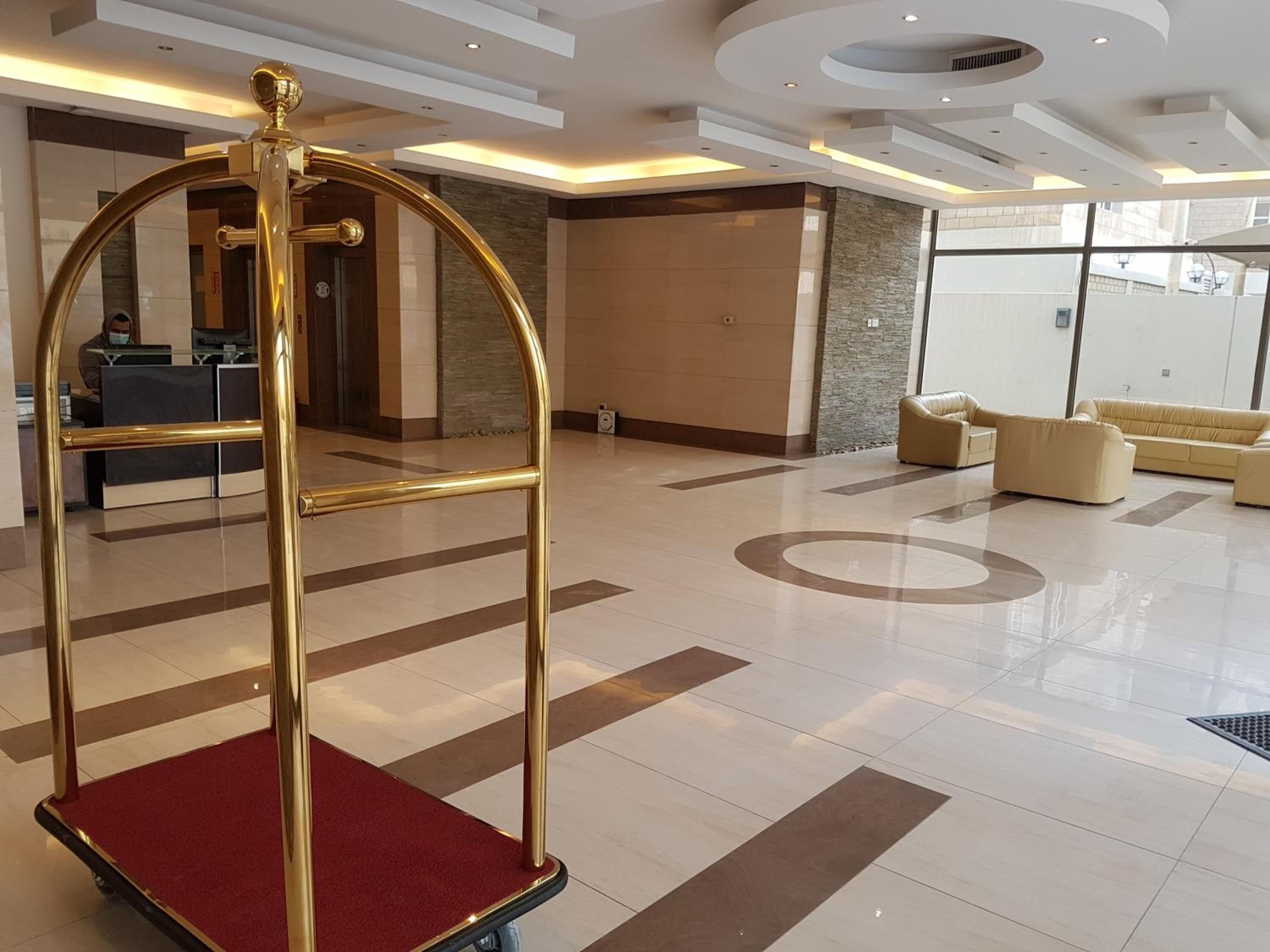 A spacious lobby with a reception desk, a gold-framed elevator, and a seating area with sofas.