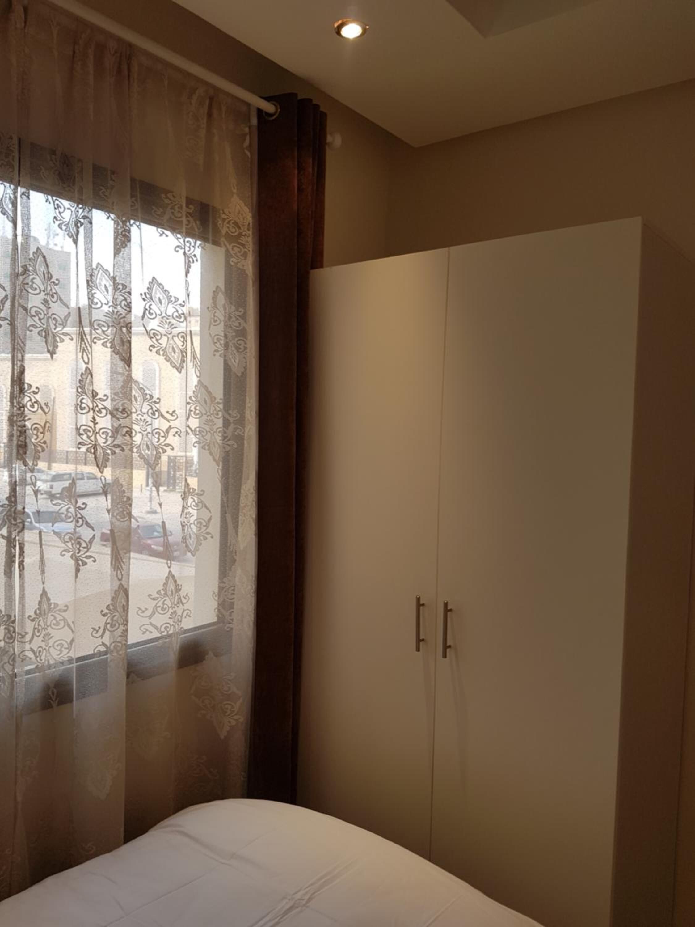 A bedroom with a bed, a wardrobe, and a window with curtains.