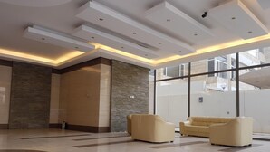 A spacious lobby with a high ceiling, recessed lighting, and a large window offering a view of the building's exterior. - Magic Suite ALMahboula 2 (Mahboula)