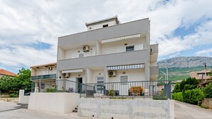 A multi-story residential building with balconies, air conditioning units, and a concrete barrier in front. - Apartment Anamaris (Solin)